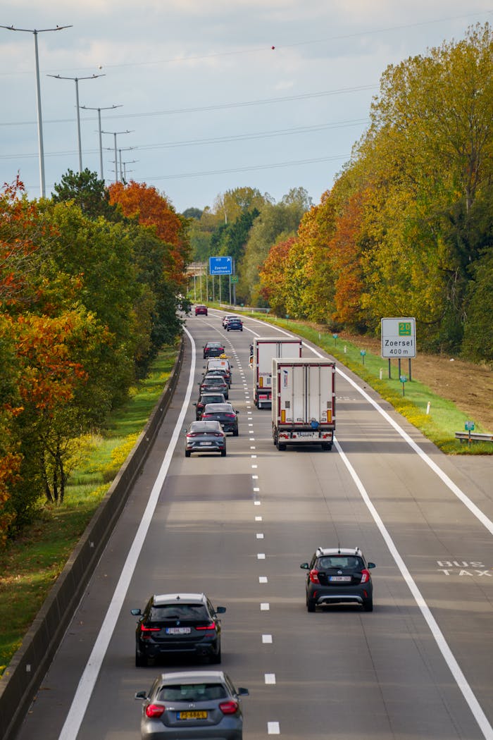 Cars and a truck on a Belgian highway surrounded by autumn foliage and clear skies.